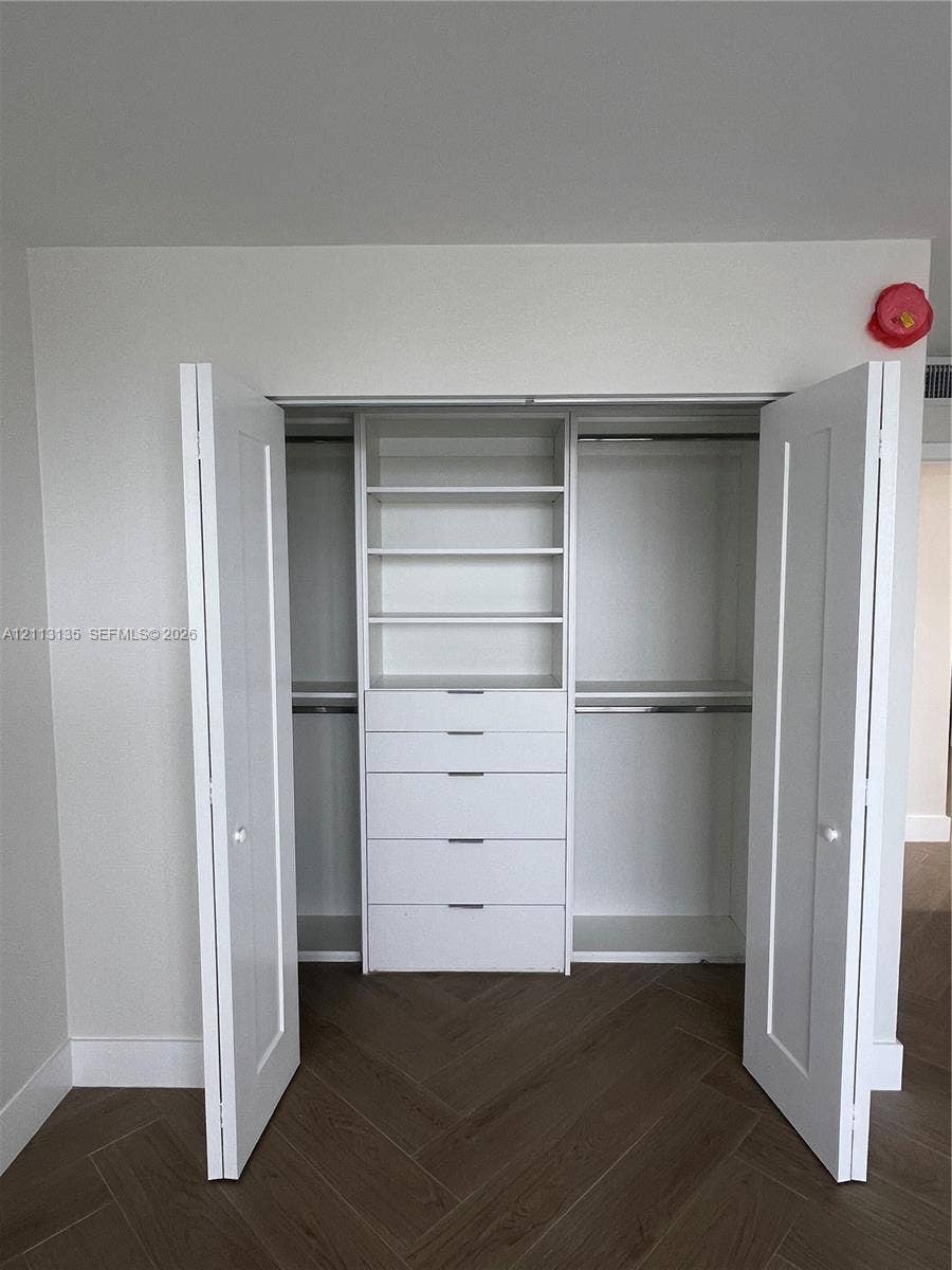 1600 S Ocean Drive, #3A, Hollywood, FL 33019 Closet featuring white dual-panel doors, built-in shelving, integrated dresser drawers, and metal hanging rods over wood-finish flooring