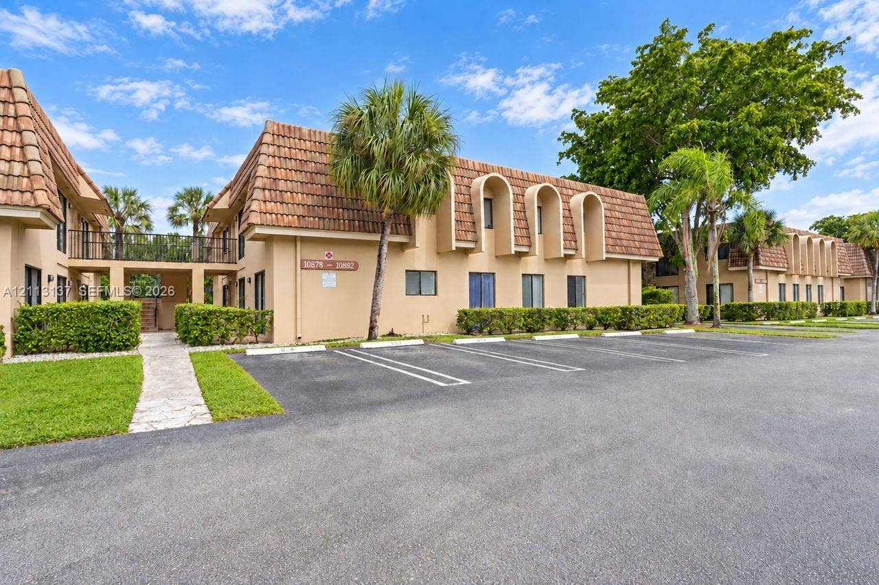 10884 Royal Palm Boulevard, #10884, Coral Springs, FL 33065 Two-story exterior featuring a clay tile roof, arched architectural accents, beige stucco finish, designated surface parking, and manicured perimeter landscaping
