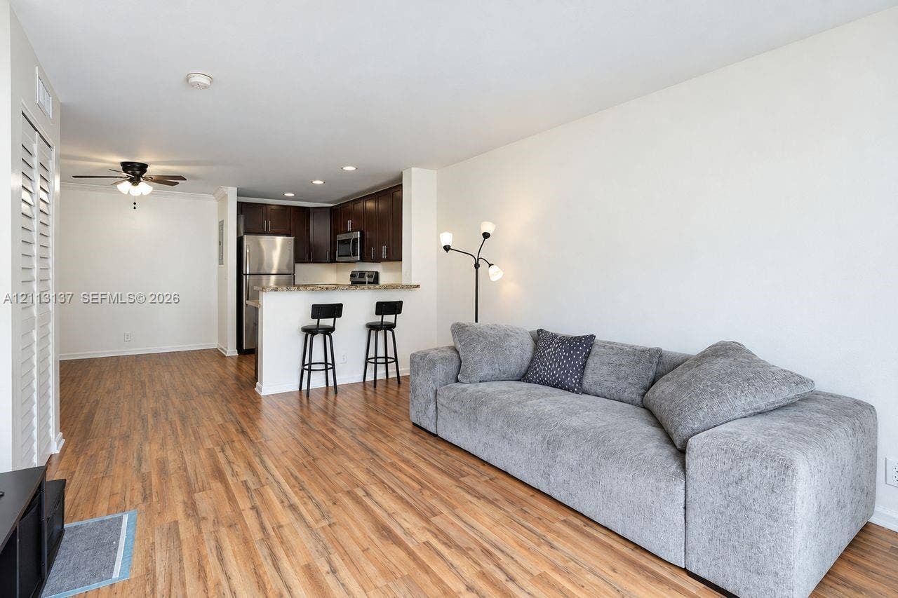 10884 Royal Palm Boulevard, #10884, Coral Springs, FL 33065 Open-concept interior featuring wood-finish flooring, dark wood cabinetry, stainless steel kitchen appliances, stone-surface breakfast bar, and recessed lighting