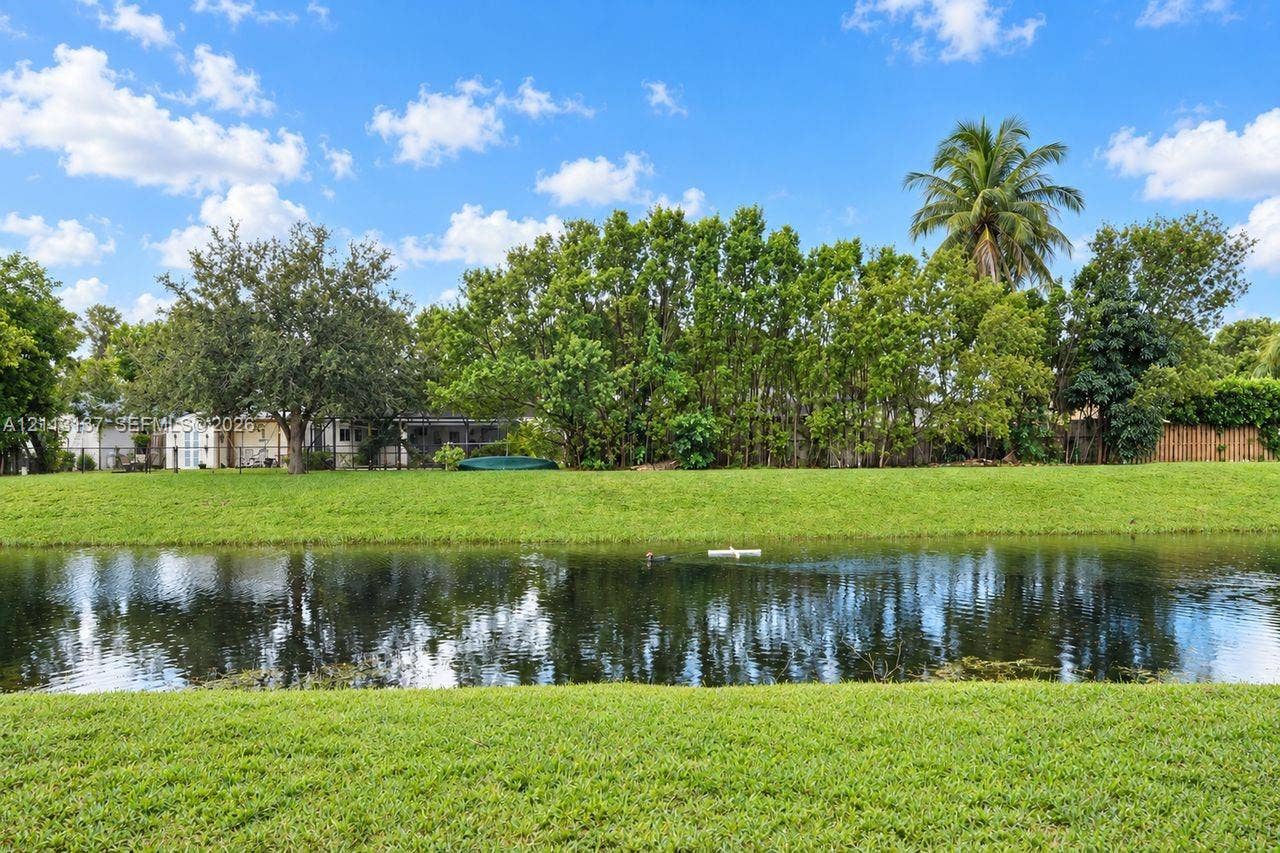 10884 Royal Palm Boulevard, #10884, Coral Springs, FL 33065 Waterfront backyard featuring a manicured lawn, mature trees, palm trees, and a wooden fence