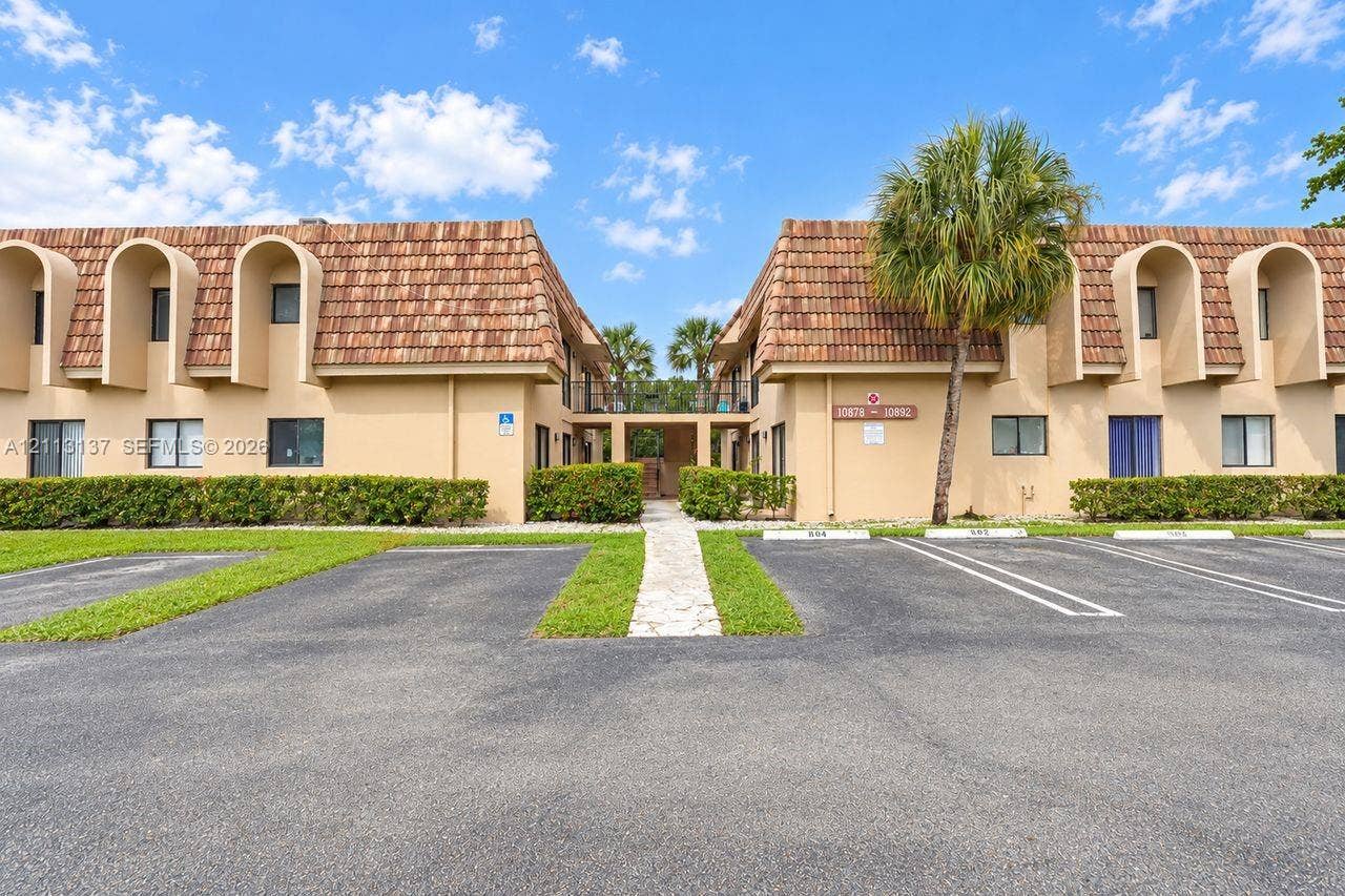 10884 Royal Palm Boulevard, #10884, Coral Springs, FL 33065 Exterior featuring a mansard roof, arched window surrounds, stucco facade, paved parking lot, and manicured landscaping