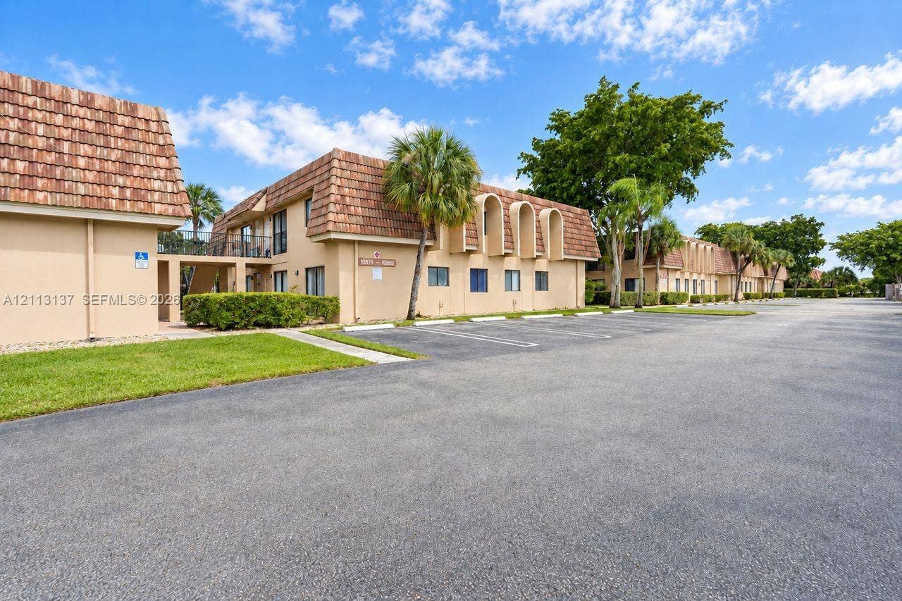 10884 Royal Palm Boulevard, #10884, Coral Springs, FL 33065 Two-story exterior featuring a clay tile roof, arched architectural details, stucco siding, paved parking area, and landscaped grounds