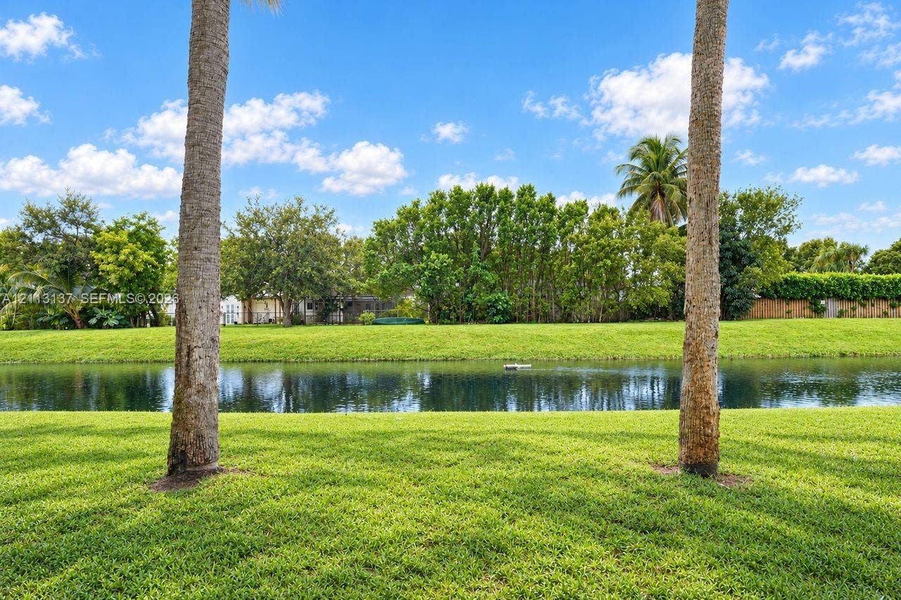 10884 Royal Palm Boulevard, #10884, Coral Springs, FL 33065 Waterfront backyard featuring a manicured lawn, palm trees, and mature landscaping