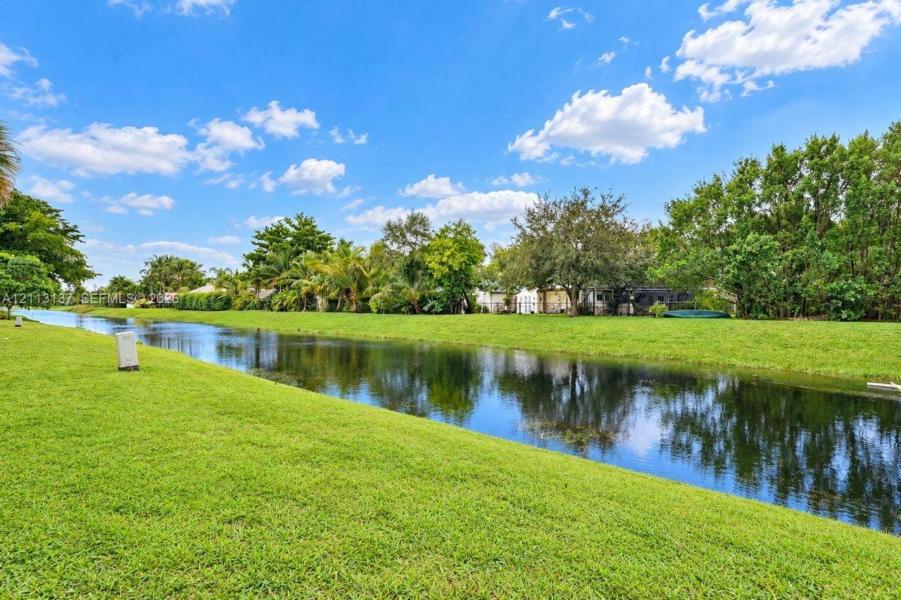 10884 Royal Palm Boulevard, #10884, Coral Springs, FL 33065 Waterfront lot featuring a grass lawn, canal frontage, and mature landscaping