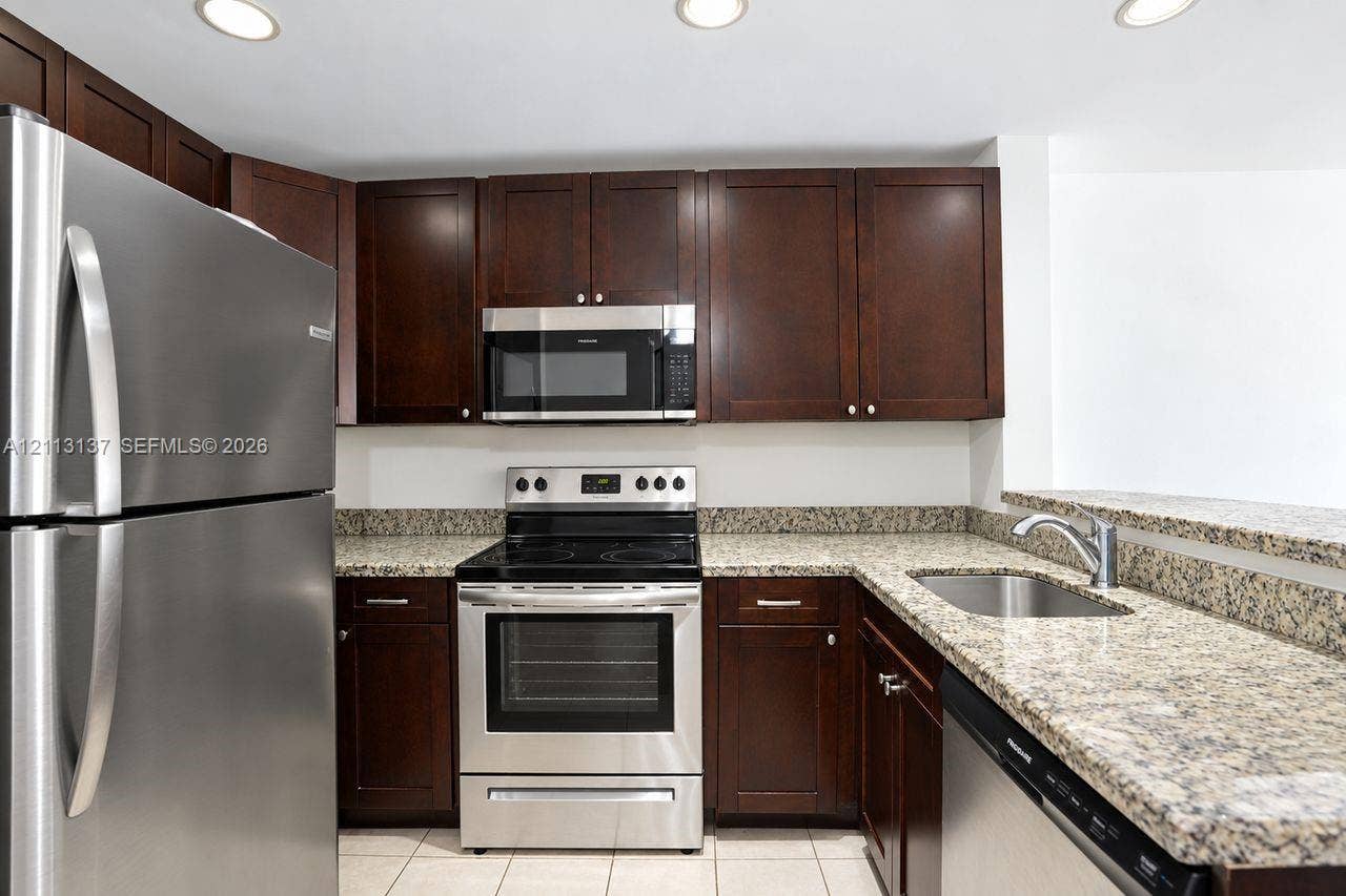 10884 Royal Palm Boulevard, #10884, Coral Springs, FL 33065 Kitchen featuring dark wood-finish cabinetry, speckled stone countertops, stainless steel appliances, recessed ceiling lighting, and tile flooring