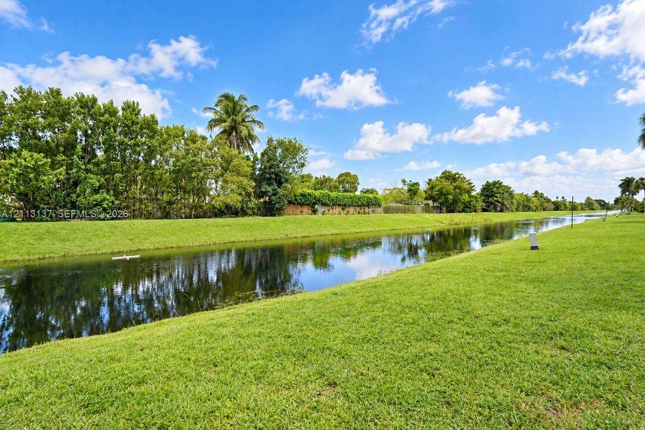 10884 Royal Palm Boulevard, #10884, Coral Springs, FL 33065 Waterfront lot featuring a grass lawn, mature trees, and palms