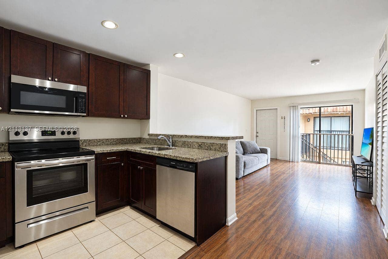 10884 Royal Palm Boulevard, #10884, Coral Springs, FL 33065 Kitchen featuring dark wood cabinetry, stone-finish countertops, stainless steel appliances, and tile flooring, paired with wood-finish flooring and a private balcony