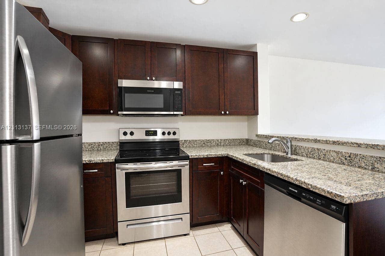 10884 Royal Palm Boulevard, #10884, Coral Springs, FL 33065 Kitchen featuring dark wood cabinetry, stone-patterned countertops, stainless steel appliances, a recessed sink, and tile flooring