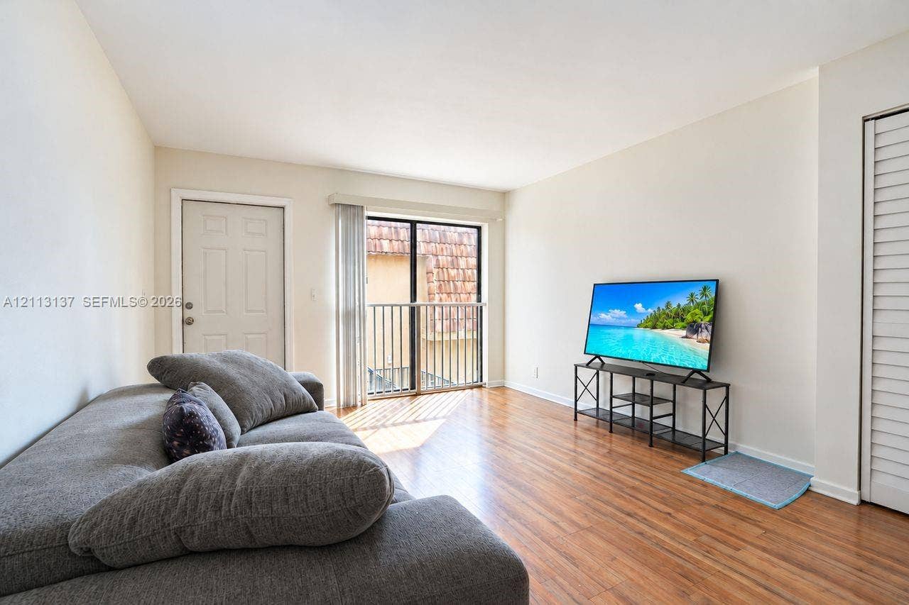 10884 Royal Palm Boulevard, #10884, Coral Springs, FL 33065 Living area featuring wood-finish flooring, neutral wall paint, and a sliding glass door providing access to a metal-railed balcony