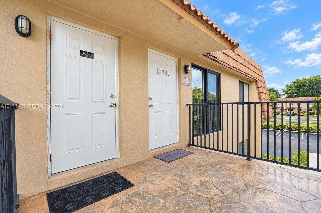 10884 Royal Palm Boulevard, #10884, Coral Springs, FL 33065 Exterior walkway featuring a stamped concrete surface, black metal railing, and light-toned stucco wall finish