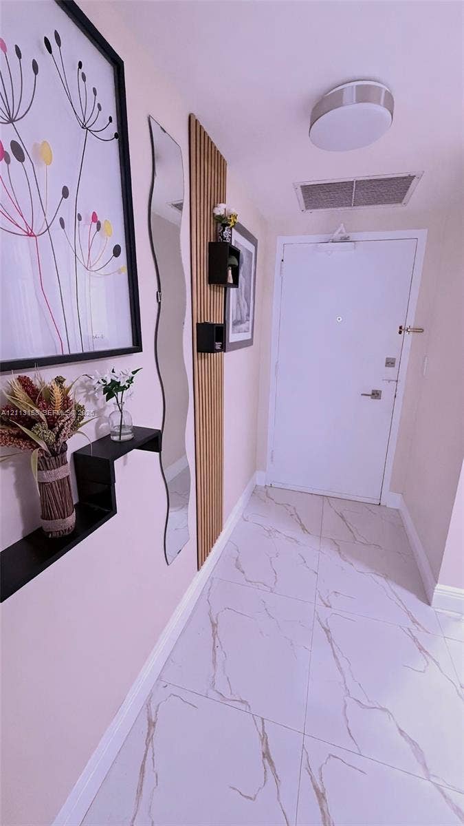 Entryway featuring large-format tile flooring with veining, vertical wood-slat accent wall, and flush-mount ceiling lighting