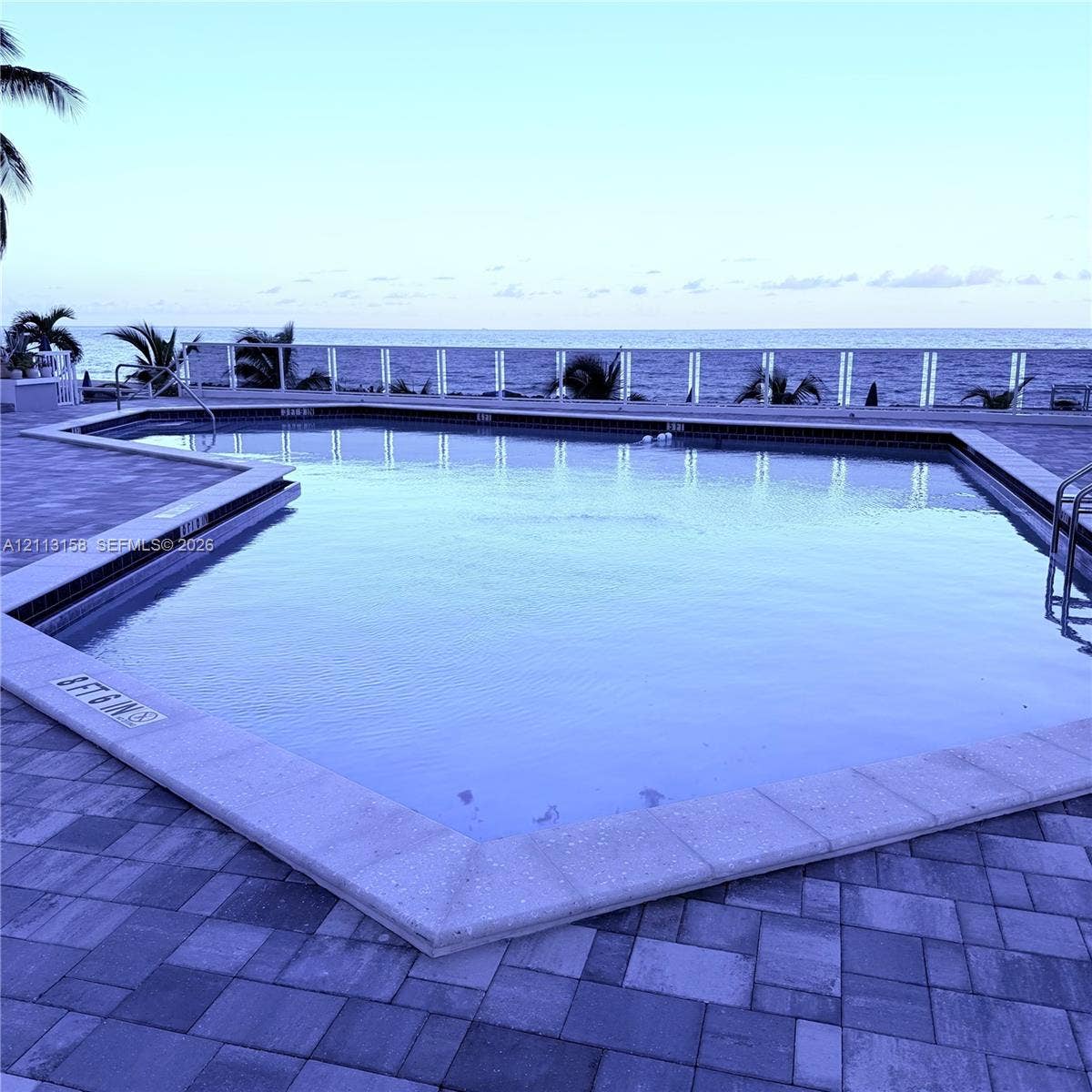Swimming pool with a stone paver deck and white railing, featuring a coastal backdrop
