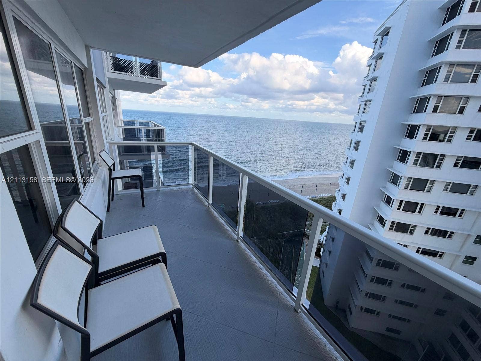 Private balcony featuring a glass-panel railing, floor-to-ceiling windows, and oceanfront exposure