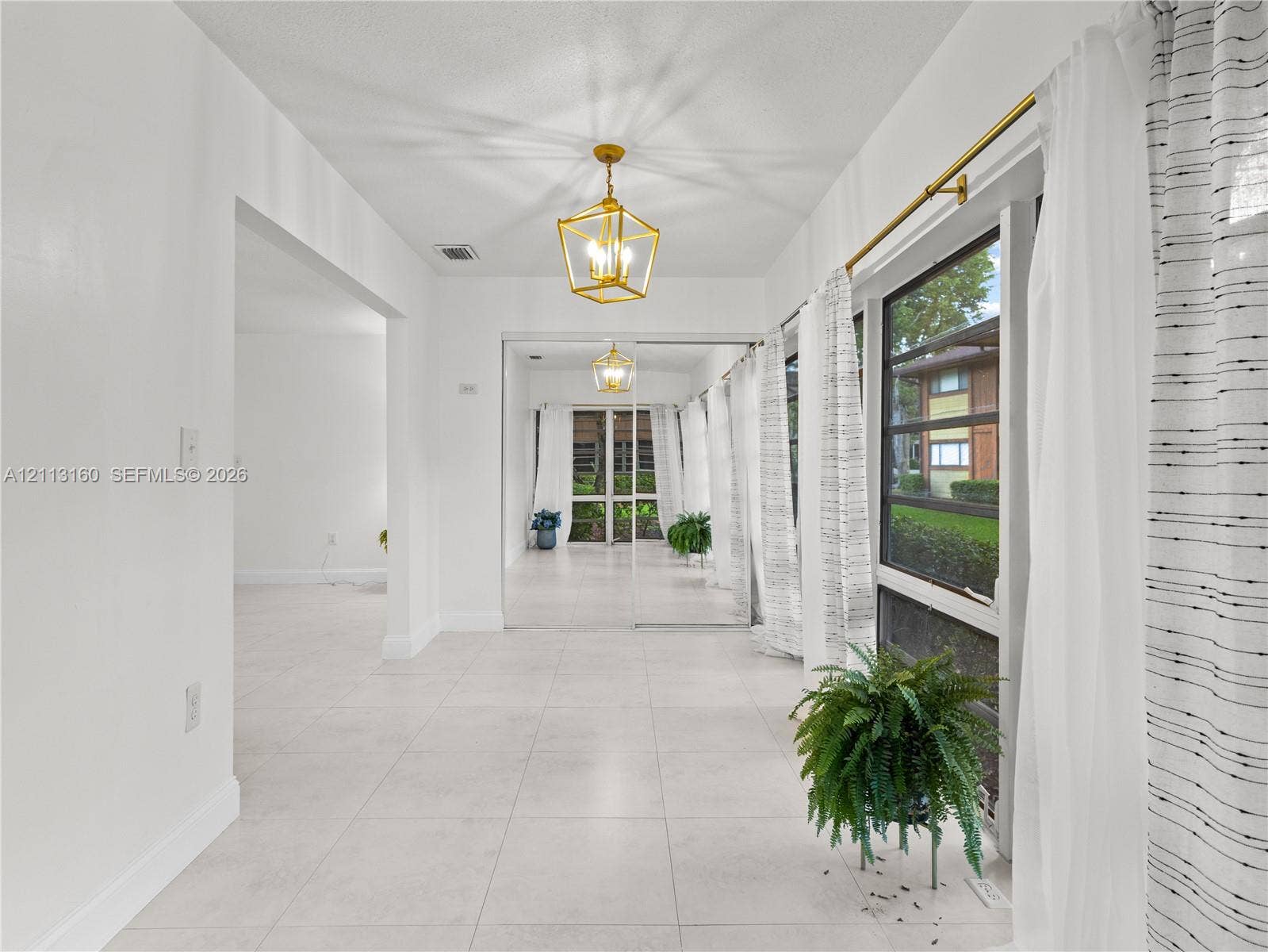 Interior space featuring large-format tile flooring, polished gold-tone geometric pendant lighting, and mirrored sliding closet doors