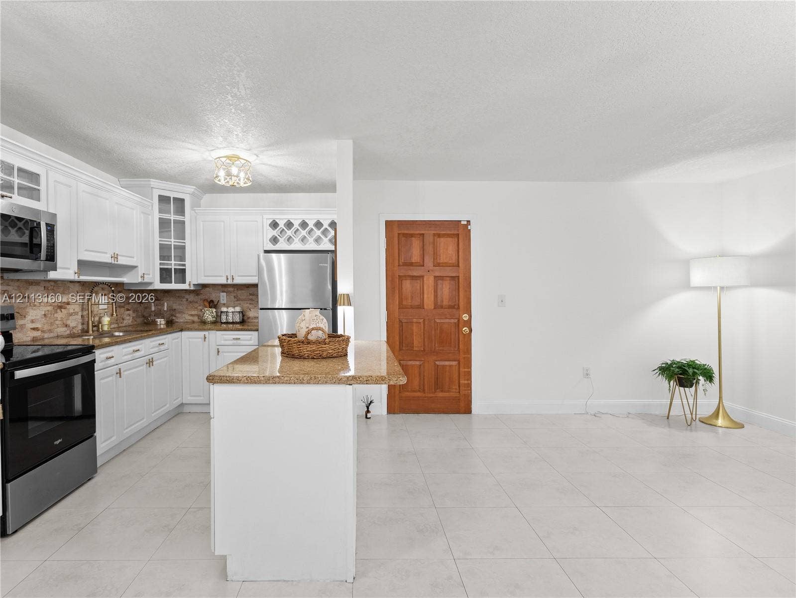 Kitchen featuring white cabinetry with glass-front display uppers, stone-finish countertops, stainless steel appliances, a center island, and a textured tile backsplash