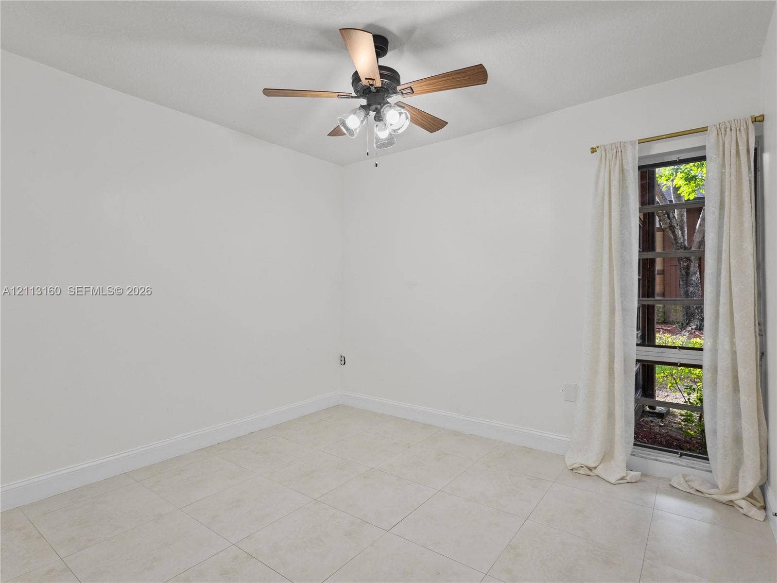 Neutral tile flooring, multi-light ceiling fan with wood-finish blades, and tall window with black-frame muntins