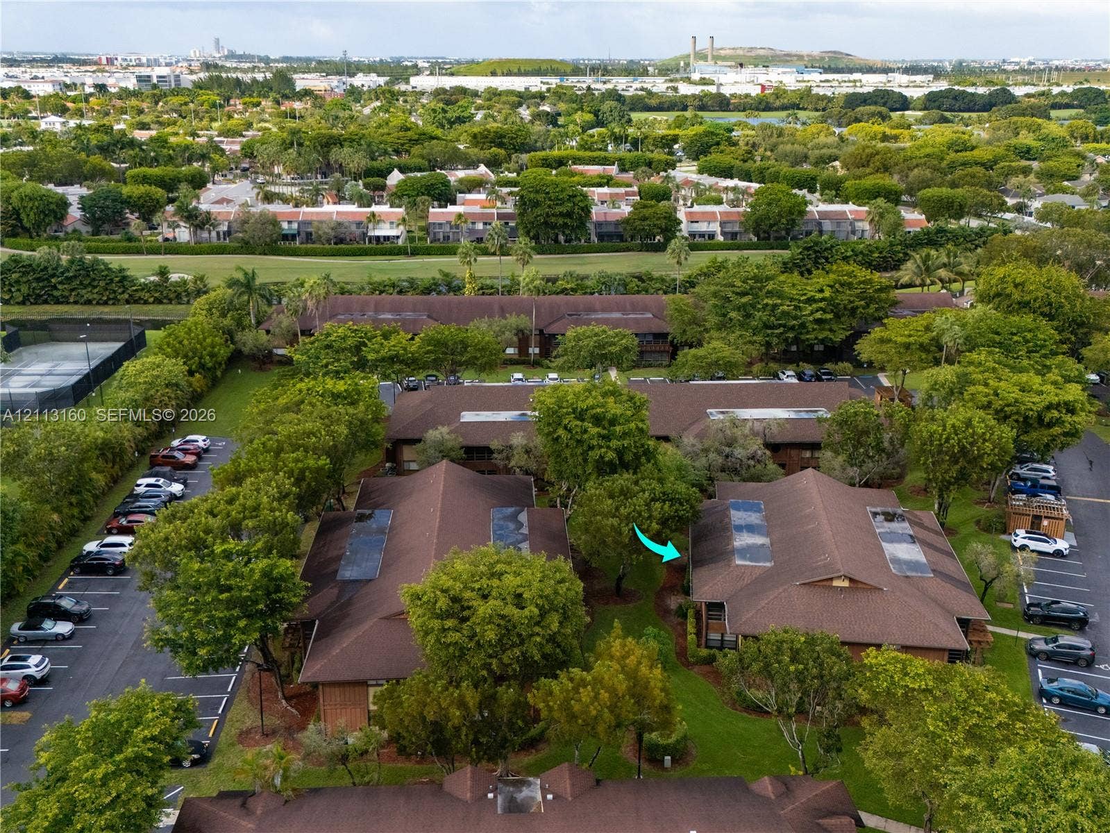 Aerial perspective featuring shingle-style roofing, skylights, surrounding mature landscaping, and dedicated surface parking