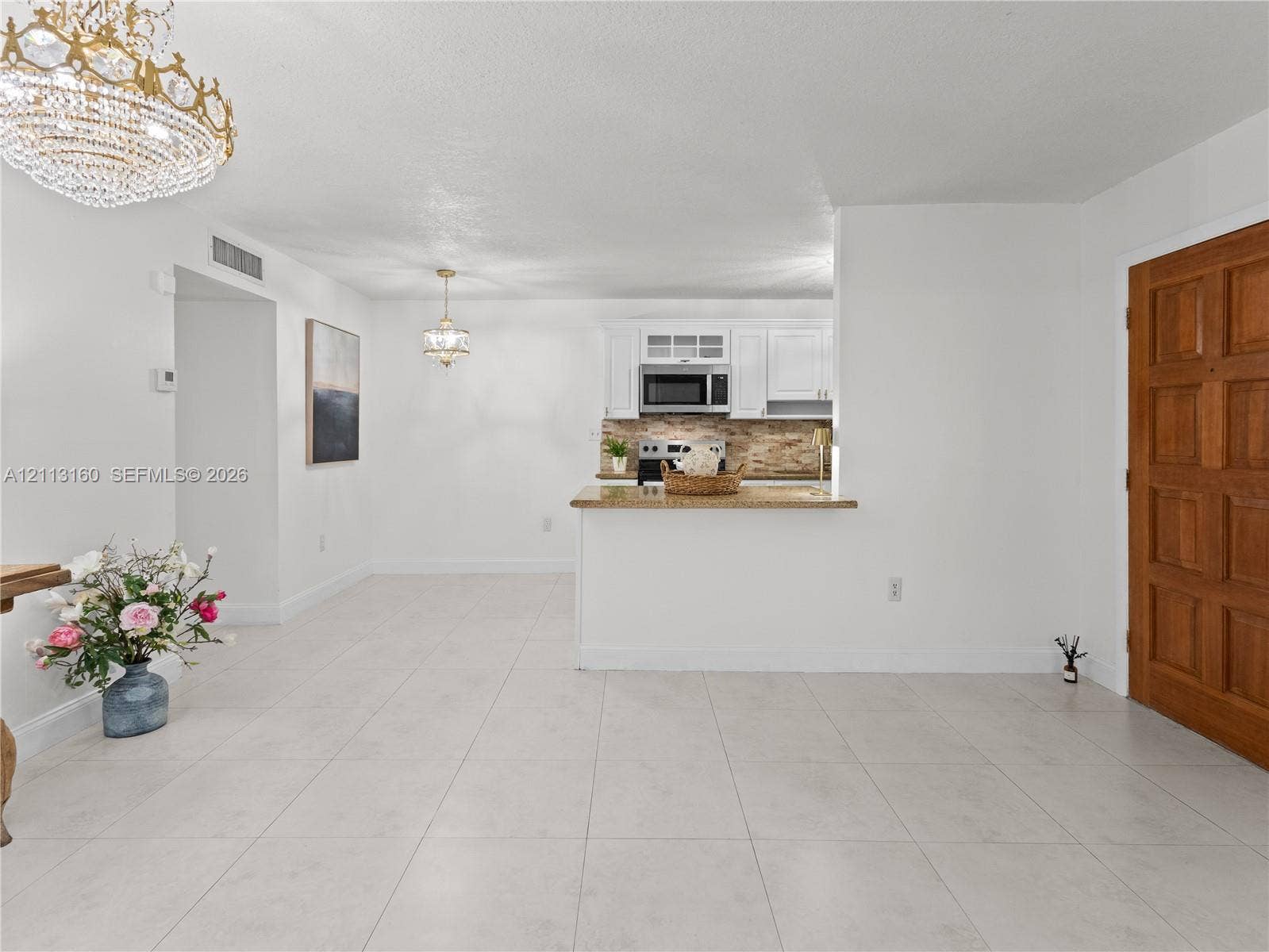 Kitchen featuring white shaker-style cabinetry, stone-surface countertops, built-in microwave, and tile flooring throughout, accented by decorative chandeliers
