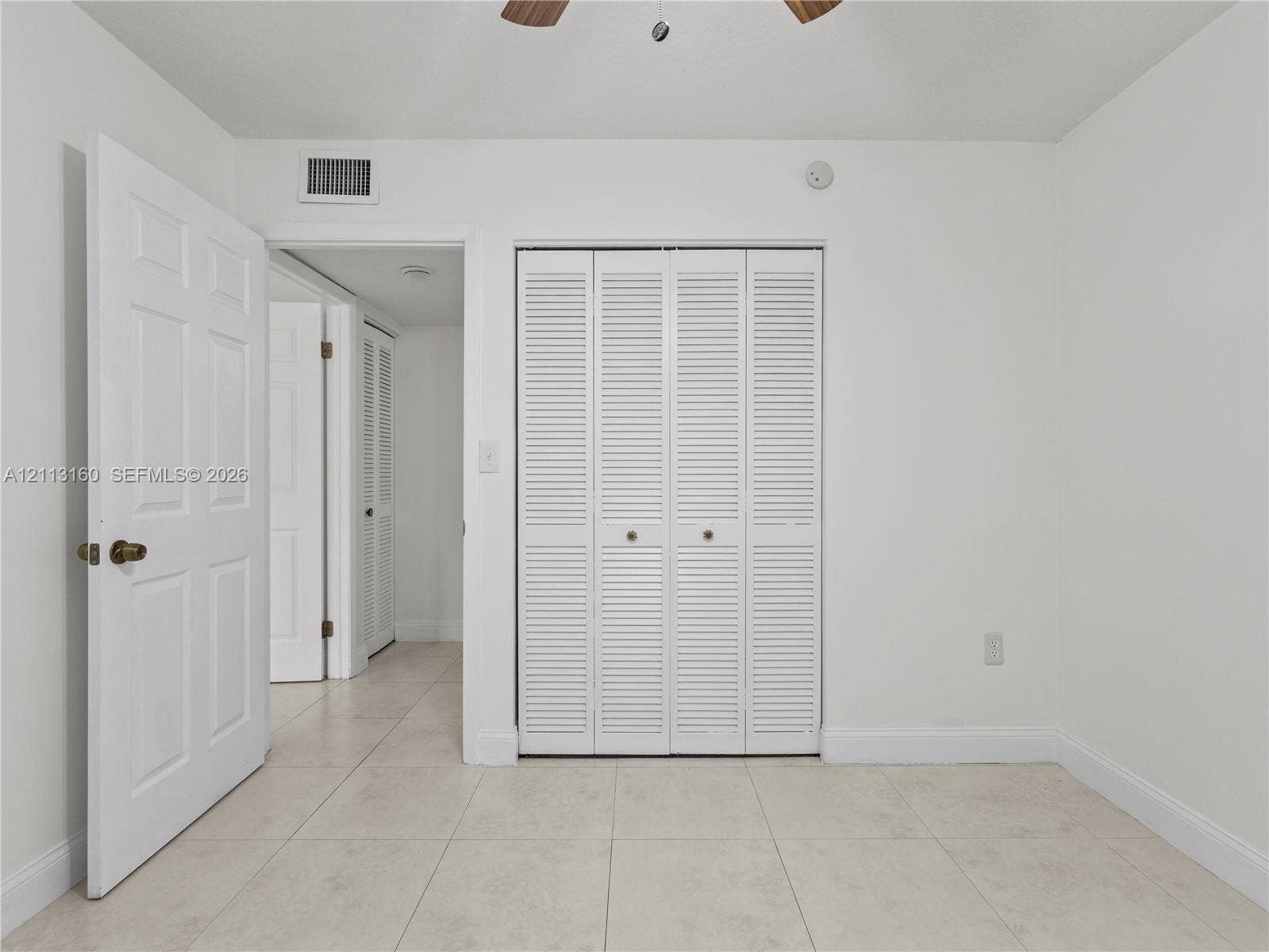 Neutral tile flooring, white six-panel interior doors, and closet featuring white bi-fold louvered doors