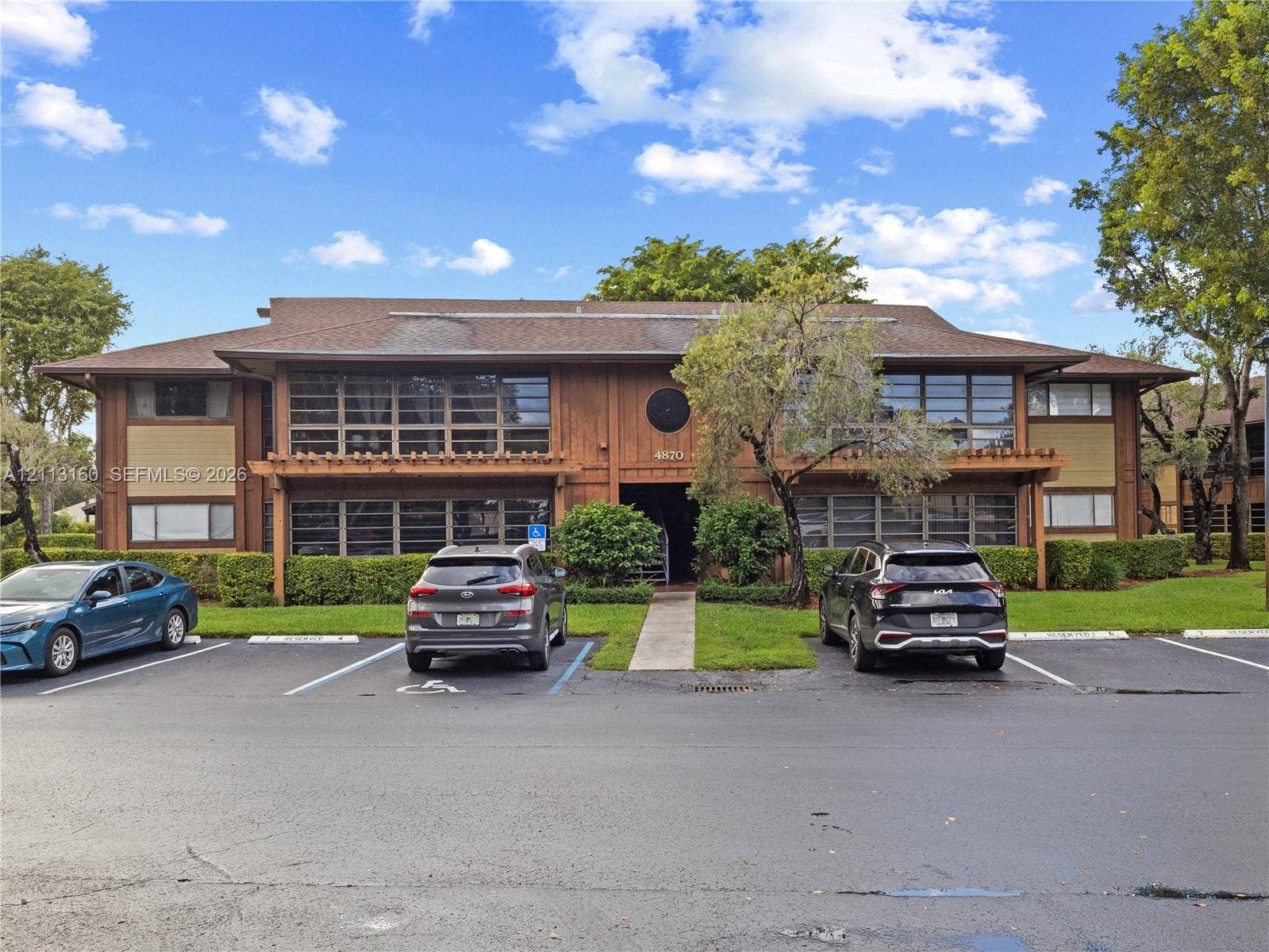 Two-story wood-siding exterior featuring expansive multi-pane windows, decorative pergola accents, shingled roofing, and paved surface parking