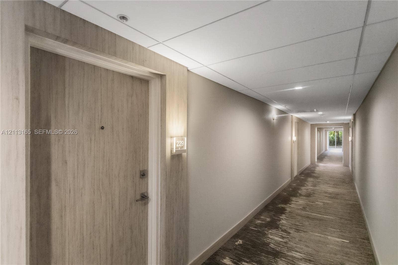 10275 Collins Avenue, #229, Bal Harbour, FL 33154 Interior hallway featuring wood-finish door cladding, recessed ceiling lighting, wall-mounted sconces, and patterned carpet flooring