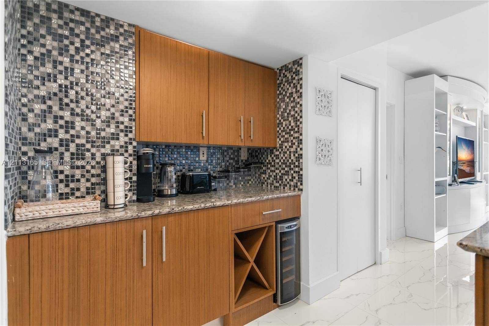 10275 Collins Avenue, #229, Bal Harbour, FL 33154 Custom cabinetry featuring integrated wine storage, stone countertops, a mosaic tile backsplash, and built-in shelving