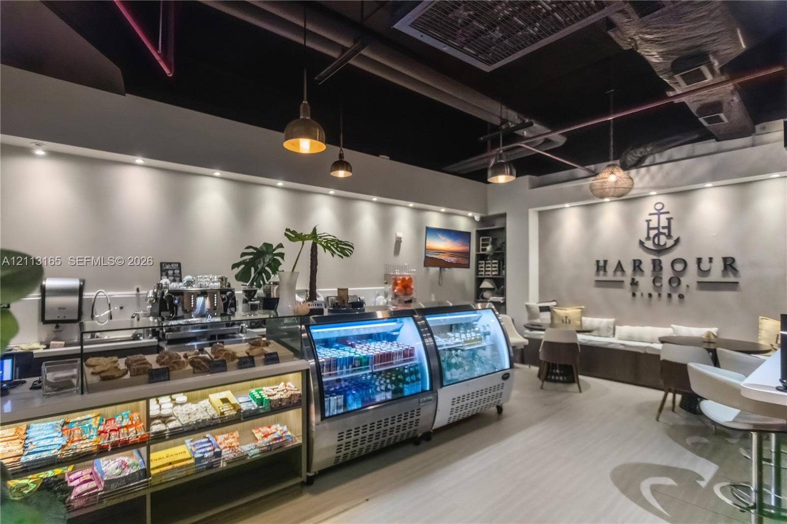 10275 Collins Avenue, #229, Bal Harbour, FL 33154 Commercial space featuring industrial-style exposed ceiling, recessed lighting, glass-front refrigerated display cases, light-toned wood-finish flooring, and built-in perimeter bench seating