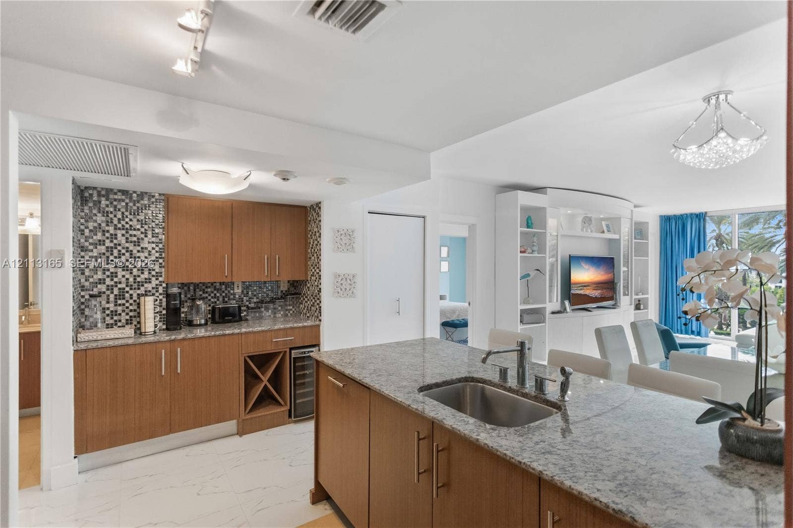 10275 Collins Avenue, #229, Bal Harbour, FL 33154 Kitchen featuring wood-finish cabinetry, stone countertops, mosaic tile backsplash, built-in wine storage, and a center island with an undermount stainless steel sink