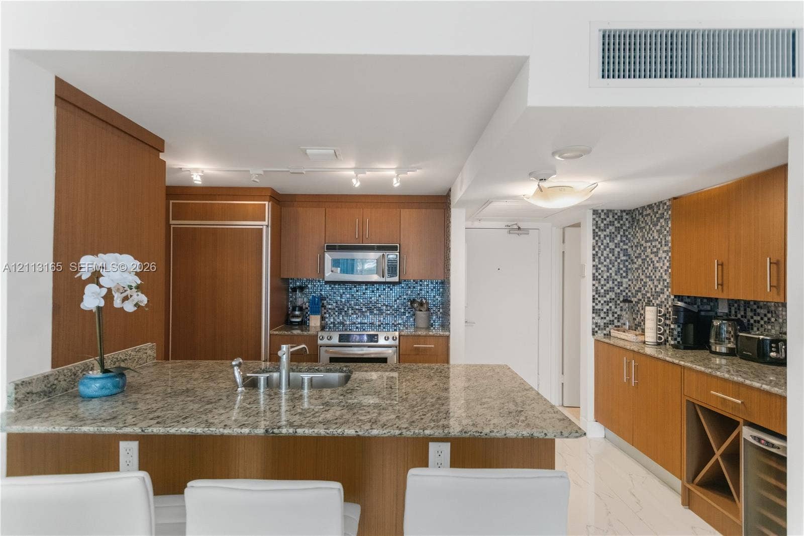 10275 Collins Avenue, #229, Bal Harbour, FL 33154 Kitchen featuring wood-finish cabinetry, stone countertops, mosaic tile backsplash, built-in stainless steel appliances, and a dedicated wine storage rack