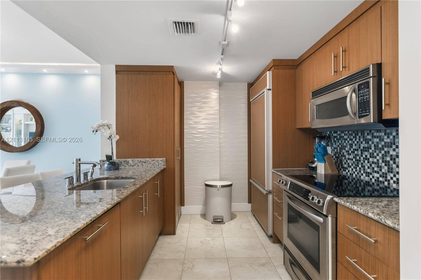 10275 Collins Avenue, #229, Bal Harbour, FL 33154 Kitchen featuring wood-finish cabinetry, stone countertops, stainless steel appliances, a tile backsplash, and stone-finish flooring