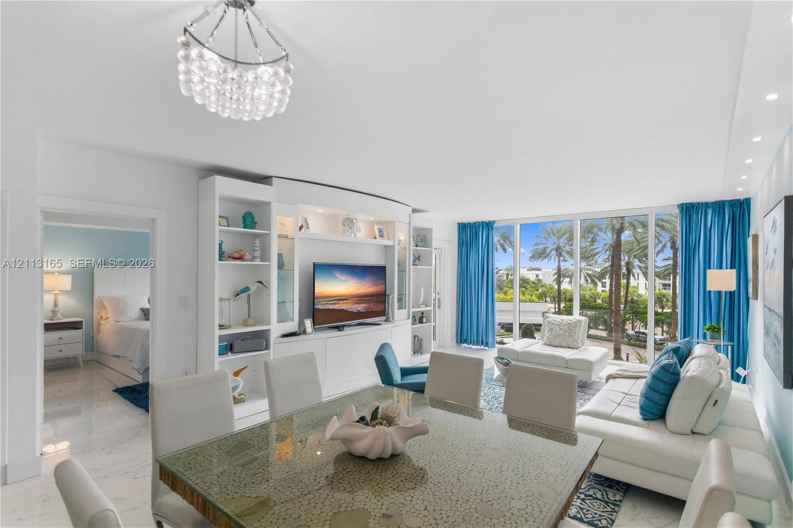 10275 Collins Avenue, #229, Bal Harbour, FL 33154 Open-concept interior featuring floor-to-ceiling windows, polished stone-finish flooring, custom built-in cabinetry with integrated shelving, and a decorative multi-tiered pendant light fixture