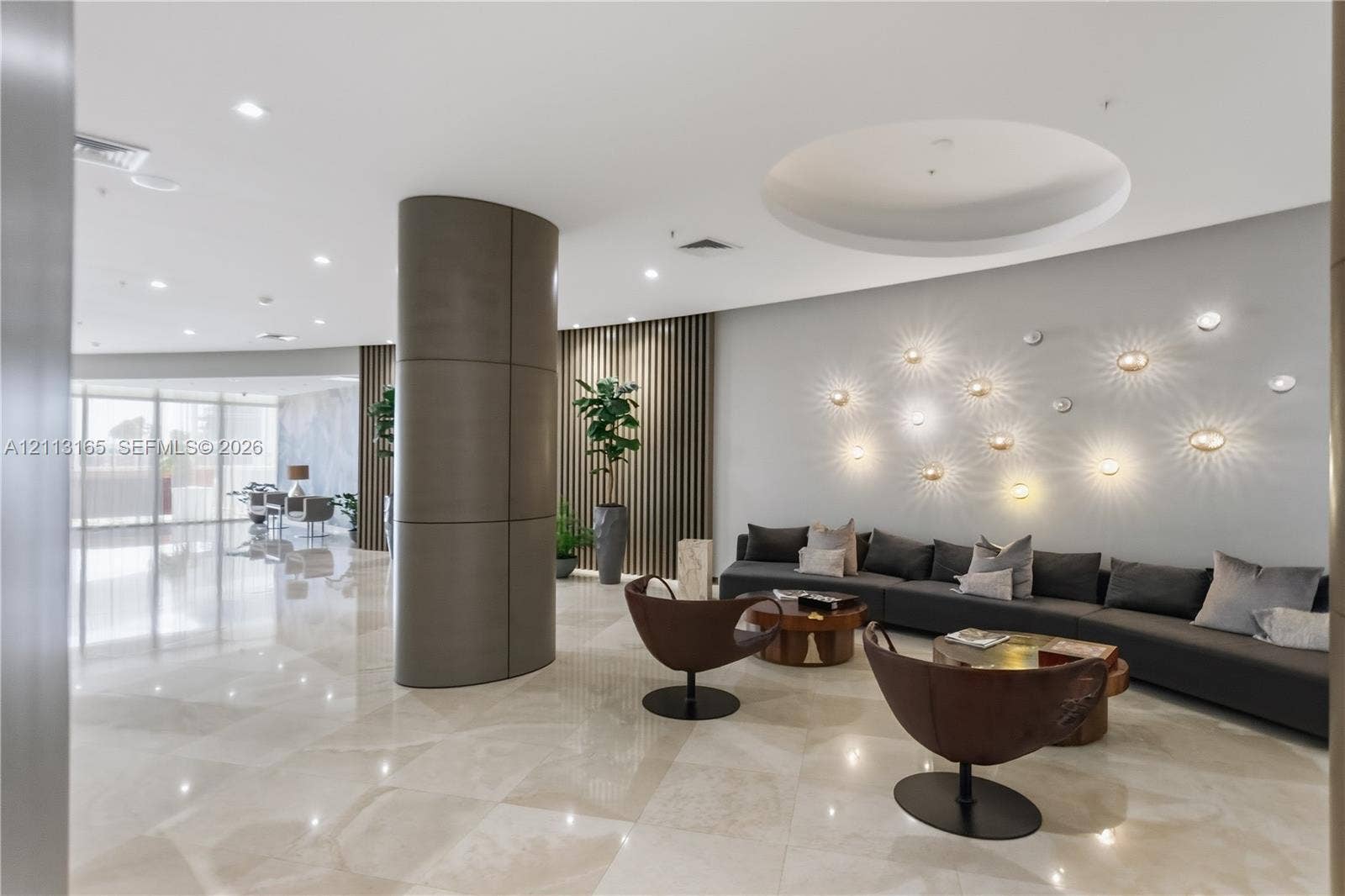 10275 Collins Avenue, #229, Bal Harbour, FL 33154 Common area featuring polished stone tile flooring, a curved architectural column, vertical wood-slat wall paneling, and recessed ceiling lighting