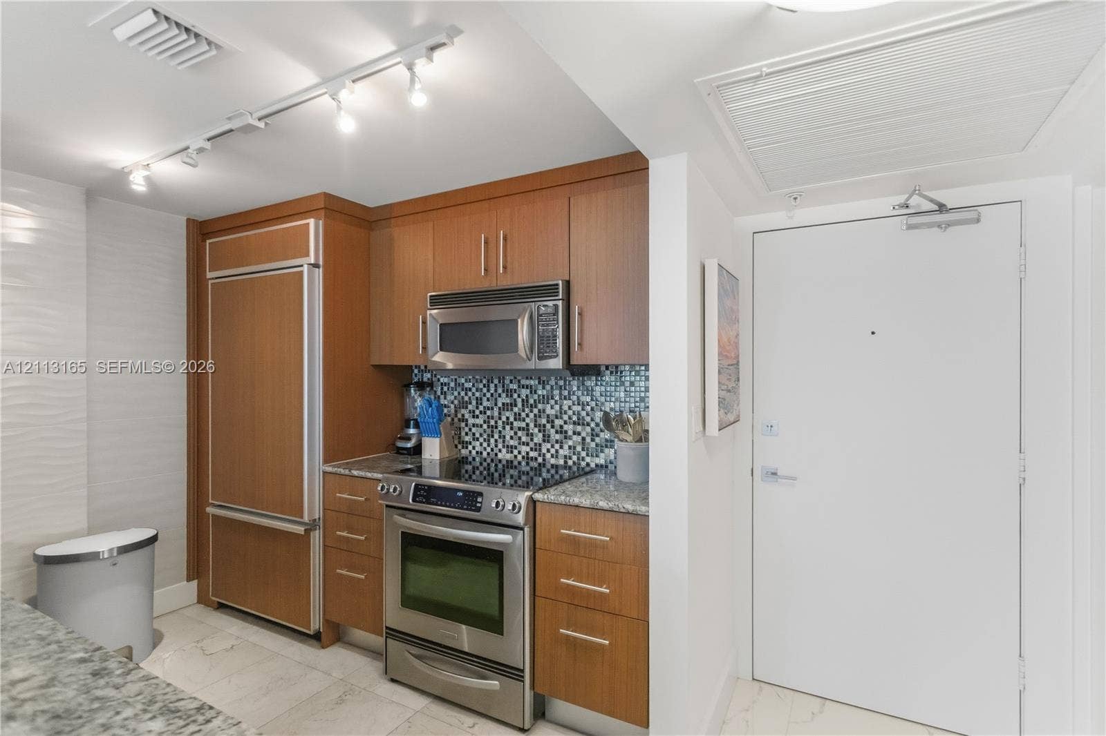10275 Collins Avenue, #229, Bal Harbour, FL 33154 Kitchen featuring wood-veneer cabinetry, integrated stainless steel refrigerator, mosaic tile backsplash, speckled stone countertops, and stainless steel range
