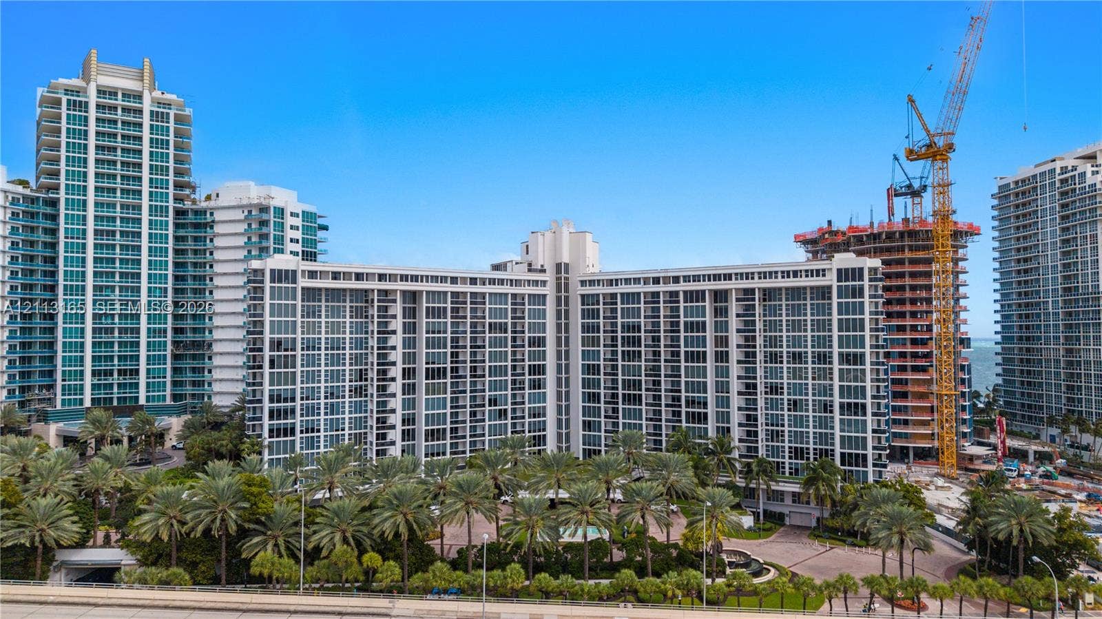 10275 Collins Avenue, #229, Bal Harbour, FL 33154 High-rise residential building featuring floor-to-ceiling glass paneling, extensive private balcony configurations, and landscaped grounds with mature palm trees