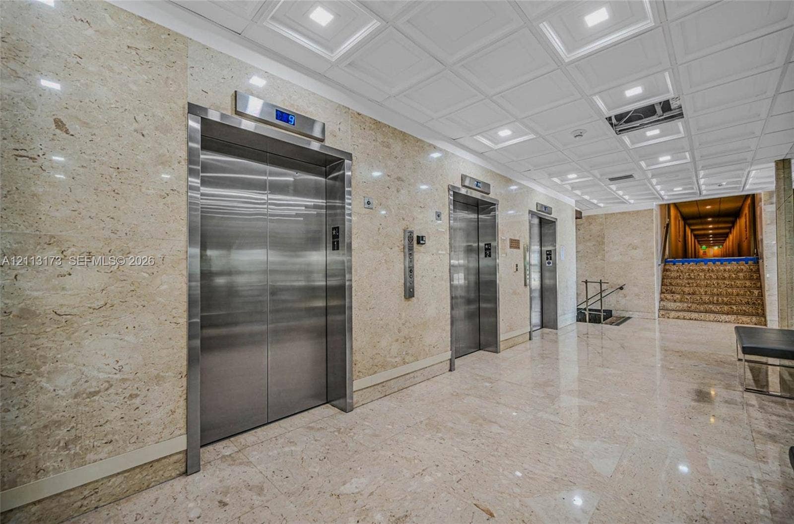 300 Bayview Drive, #1614, Sunny Isles Beach, FL 33160 Polished stone wall cladding, stainless steel elevator doors, recessed ceiling lighting, coffered ceiling detail, and polished stone tile flooring