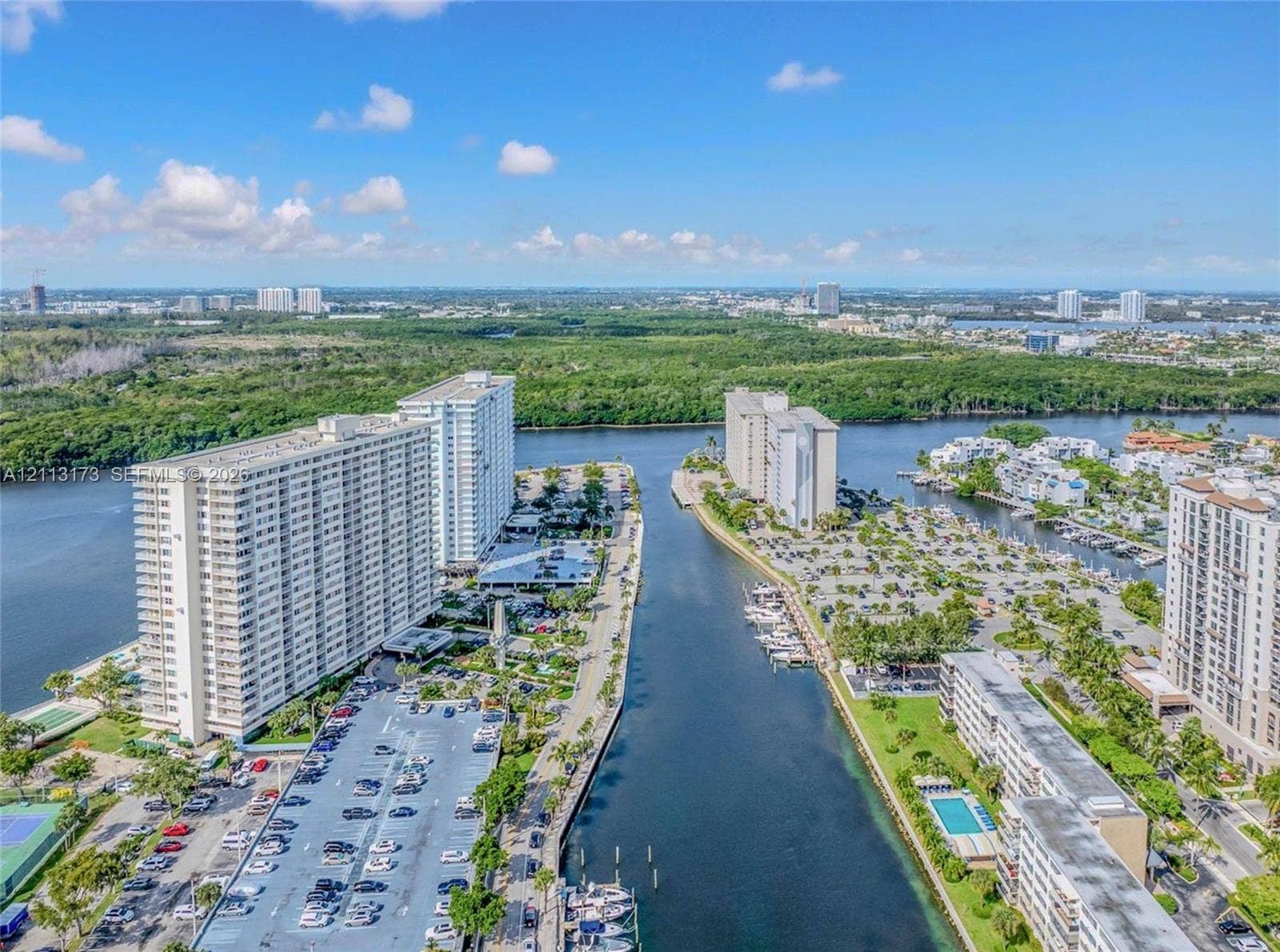 300 Bayview Drive, #1614, Sunny Isles Beach, FL 33160 Aerial perspective featuring waterfront high-rise residential buildings, a central navigable waterway, on-site parking lots, and coastal landscaping