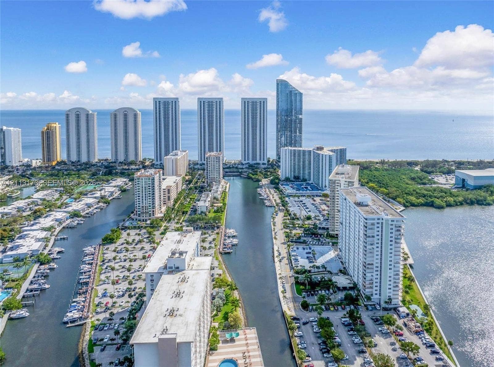 300 Bayview Drive, #1614, Sunny Isles Beach, FL 33160 Aerial perspective of high-rise structures situated along an inlet, featuring direct water frontage, private boat docking, paved parking areas, and coastal surroundings