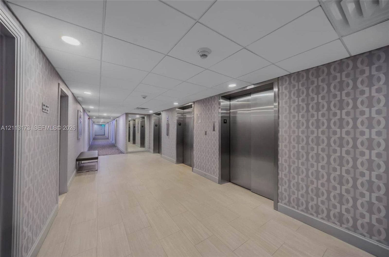 300 Bayview Drive, #1614, Sunny Isles Beach, FL 33160 Hallway featuring tile flooring, patterned wall coverings, recessed lighting, and stainless steel elevator doors