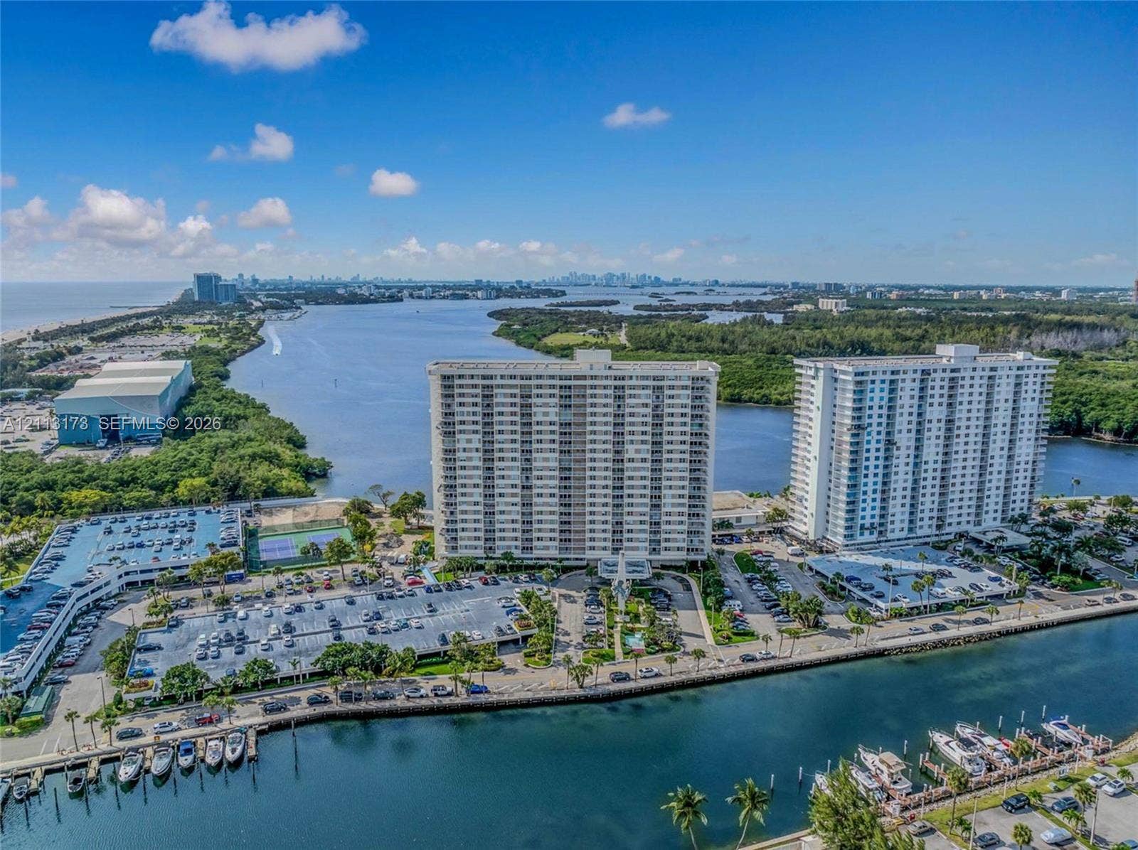 300 Bayview Drive, #1614, Sunny Isles Beach, FL 33160 Aerial perspective of coastal high-rise buildings featuring waterfront positioning, private boat slips, paved parking structures, and outdoor tennis courts