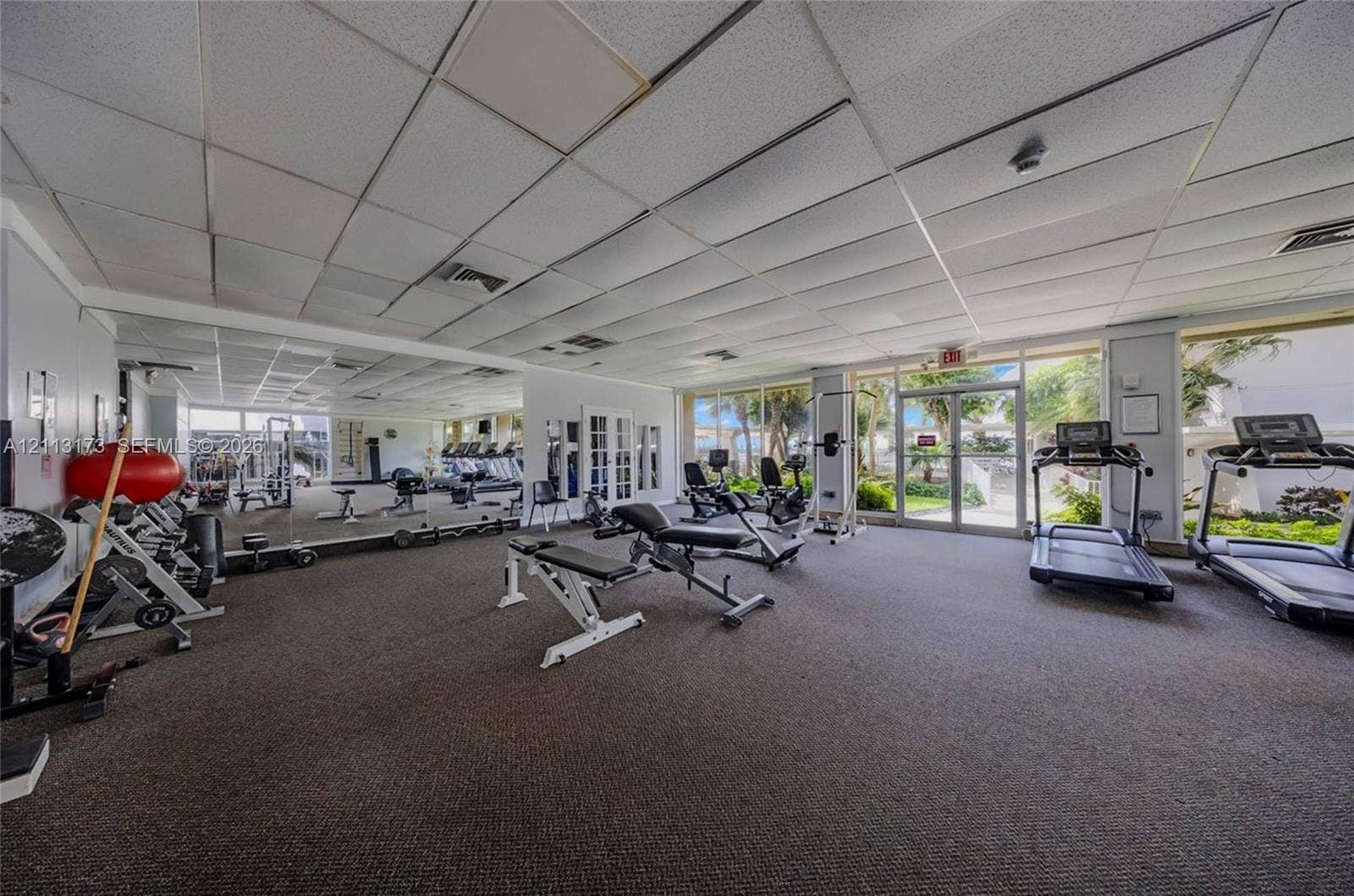 300 Bayview Drive, #1614, Sunny Isles Beach, FL 33160 Fitness center featuring wall-to-wall mirrors, recessed drop-ceiling grid, carpeted flooring, and floor-to-ceiling windows with external landscape access