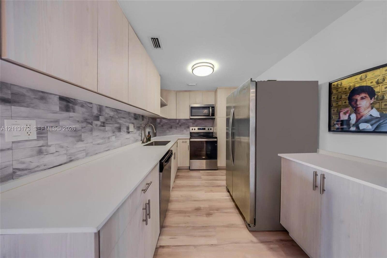 300 Bayview Drive, #1614, Sunny Isles Beach, FL 33160 Galley kitchen featuring light-toned cabinetry, solid surface countertops, a textured stone-patterned backsplash, stainless steel appliances, and wood-finish flooring