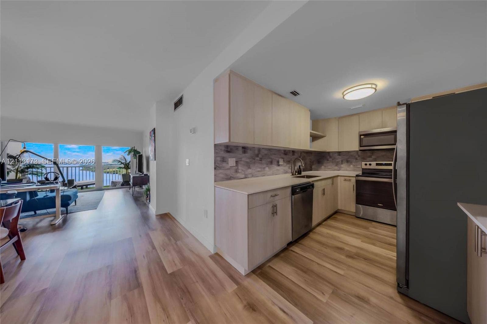 300 Bayview Drive, #1614, Sunny Isles Beach, FL 33160 Kitchen featuring light-finish cabinetry, stone-texture backsplash, solid-surface countertops, and stainless steel appliances, set against wood-finish flooring