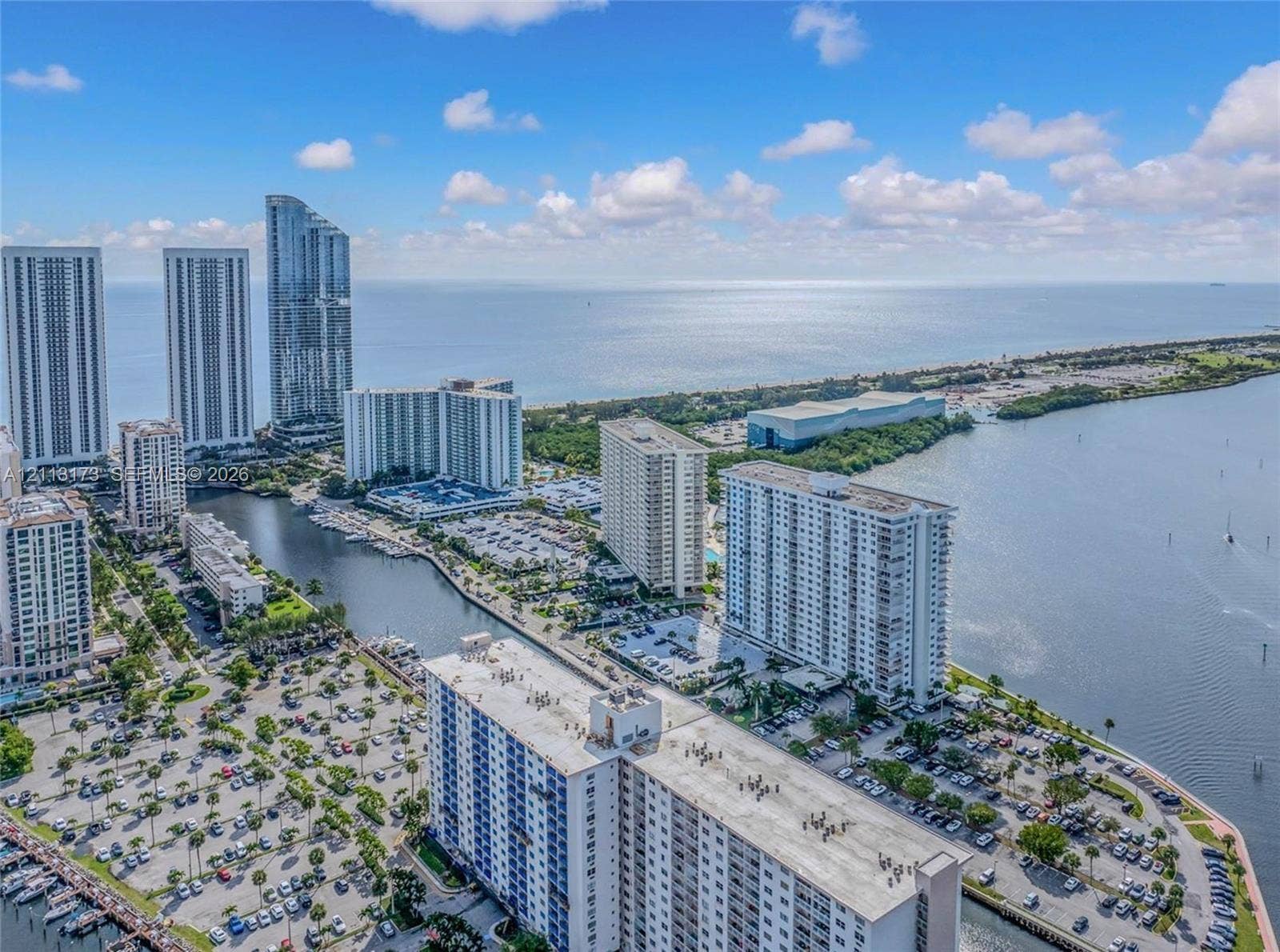 300 Bayview Drive, #1614, Sunny Isles Beach, FL 33160 Aerial perspective of coastal high-rise development featuring waterfront proximity, deep-water canal access, paved surface parking, and proximity to the Atlantic Ocean