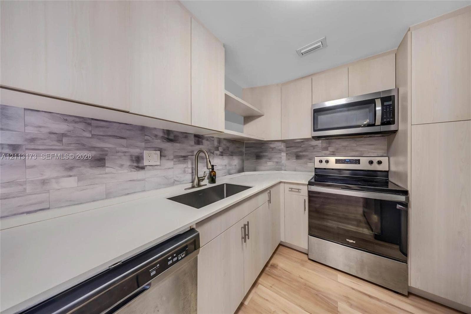 300 Bayview Drive, #1614, Sunny Isles Beach, FL 33160 Kitchen featuring light-toned cabinetry, solid surface countertops, stainless steel appliances, and a horizontal tile backsplash
