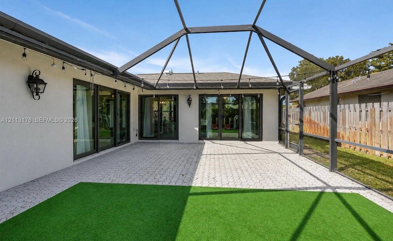 4391 NW 112th Avenue, Coral Springs, FL 33065 Screen-enclosed patio featuring a paver surface, artificial turf, metal structural framing, and exterior wall-mounted light fixtures with multi-panel glass sliding doors
