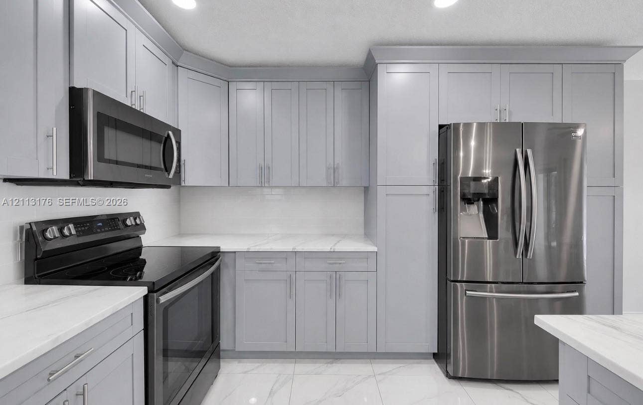 4391 NW 112th Avenue, Coral Springs, FL 33065 Kitchen featuring light grey shaker-style cabinetry, white countertops with grey veining, stainless steel appliances, and large-format tile flooring