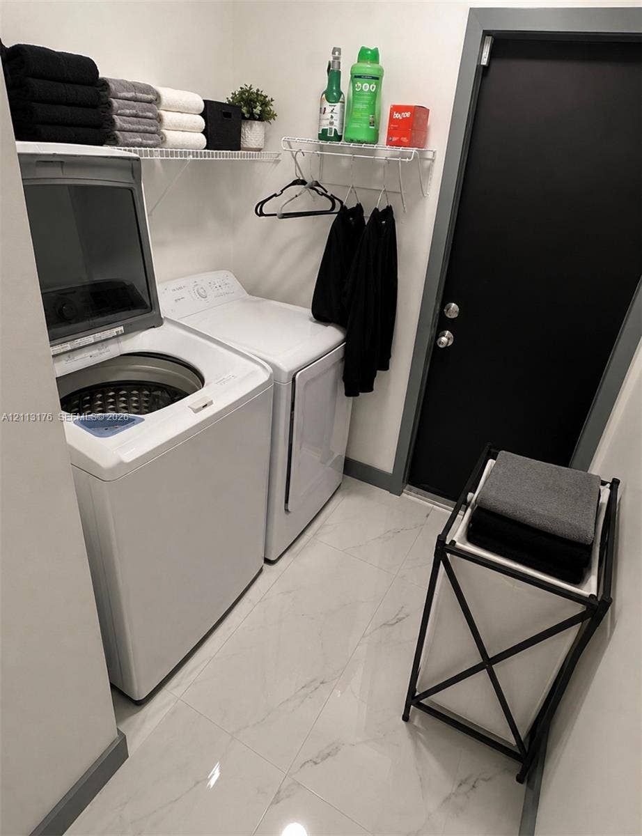 4391 NW 112th Avenue, Coral Springs, FL 33065 Laundry room featuring large-format porcelain tile flooring, top-load washer and dryer, white wire shelving, and a solid-core black door with metallic hardware
