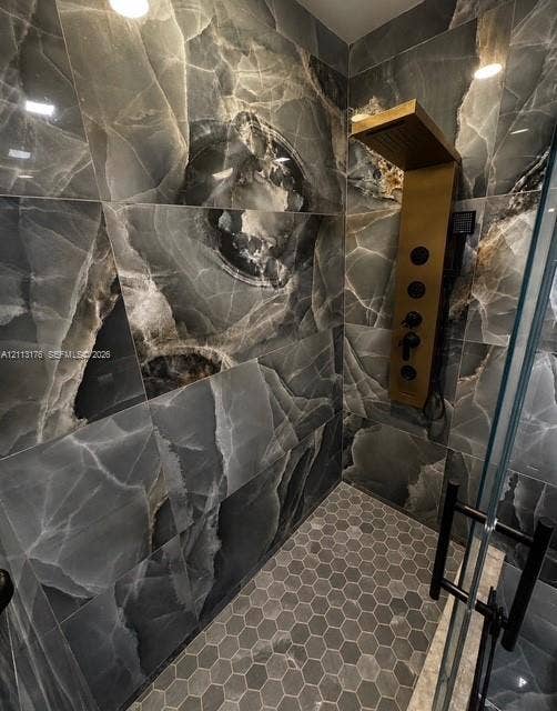 4391 NW 112th Avenue, Coral Springs, FL 33065 Walk-in shower featuring large-format dark stone-finish wall tile, a gold-tone wall-mounted shower panel, hexagonal floor tile, and a glass door with matte black hardware