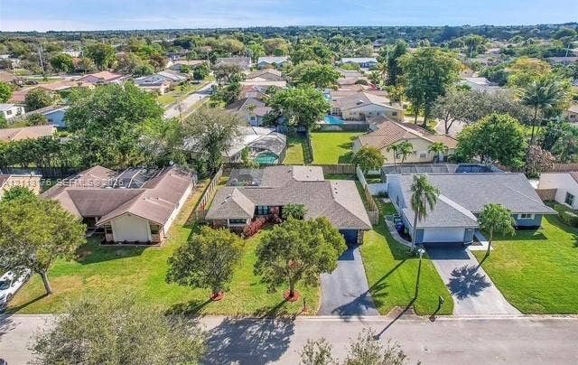 4391 NW 112th Avenue, Coral Springs, FL 33065 Aerial perspective of a single-story residence featuring a shingled roof, an attached garage, a paved driveway, and established landscaping including mature trees and lawn