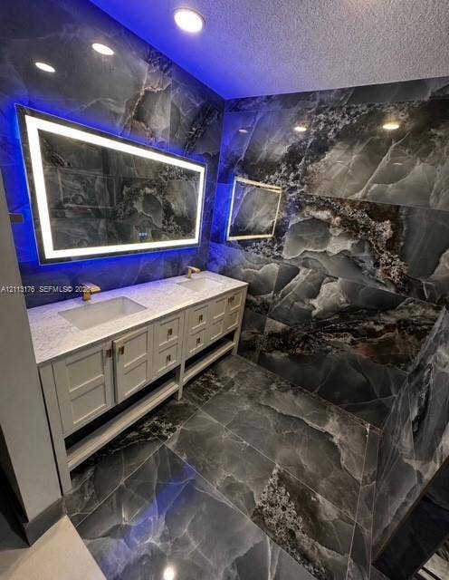 4391 NW 112th Avenue, Coral Springs, FL 33065 Dual-vanity cabinetry with a light-toned stone countertop, dual rectangular undermount sinks, gold-tone fixtures, and large-format dark-veined stone-finish wall and floor tile